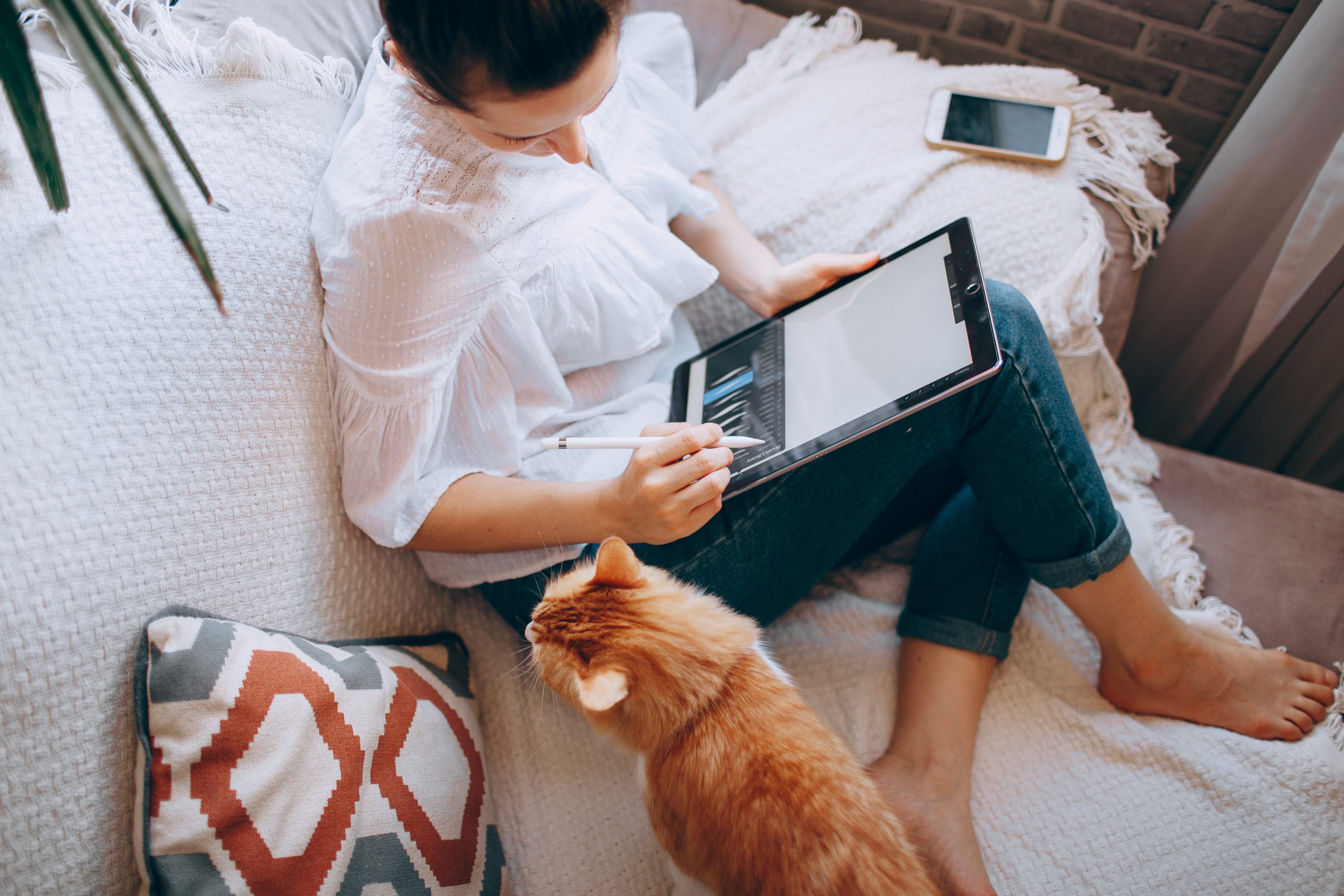 Woman working with a tablet next to her cat on a couch