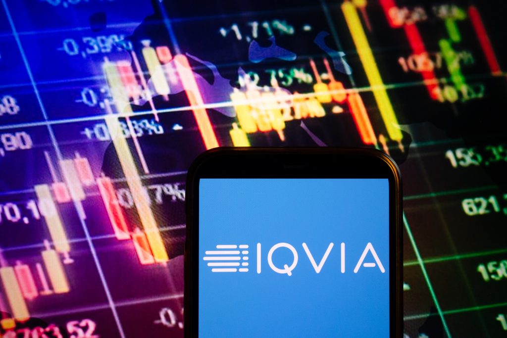 IQVIA logo on cellphone screen in front of a stock-market graph